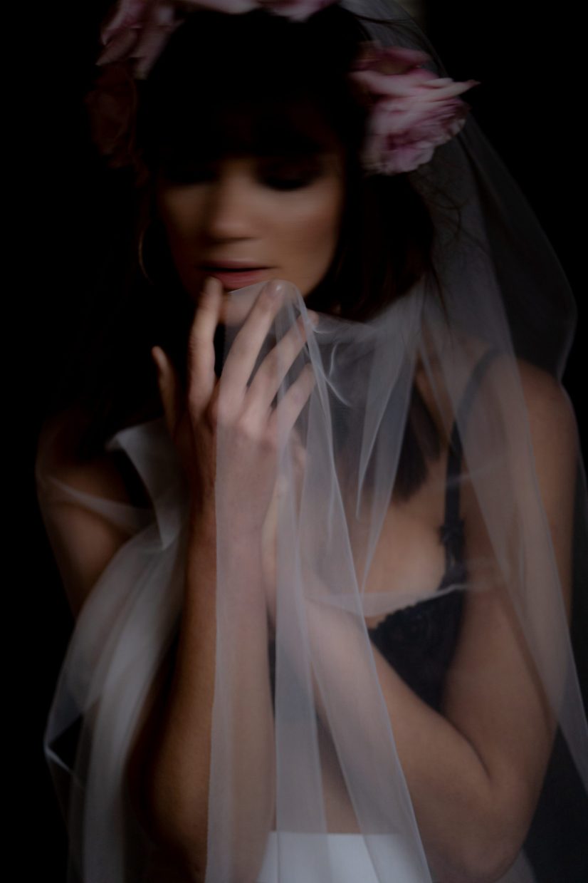 A bride with a sheer veil and closed eyes, softly lit against shadow
